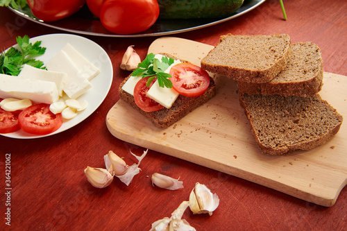 healthy food - fresh bread and feta cheese on a wooden background, tomatoes, greens and vegetables