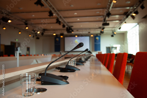 A large meeting venue with microphones and a big display in the background