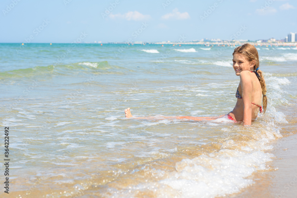 A girl of ten years old sits in the water on an empty seashore A girl of ten years old sits in the water on an empty seashore