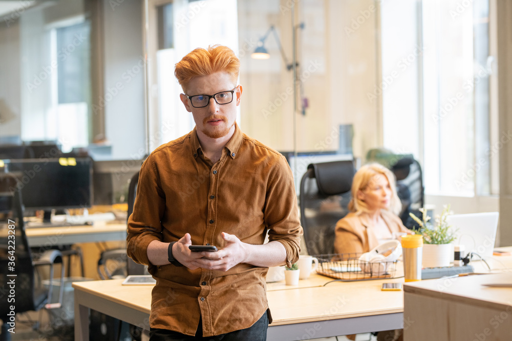 Fototapeta premium Young contemporary businessman in eyeglasses and casualwear using mobile phone