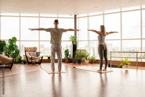 Back view of young active couple standing on mats with their arms outstretched