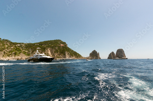 Boats visiting the coast of the island of Capri, with the Faraglioni in the background, Italy.
