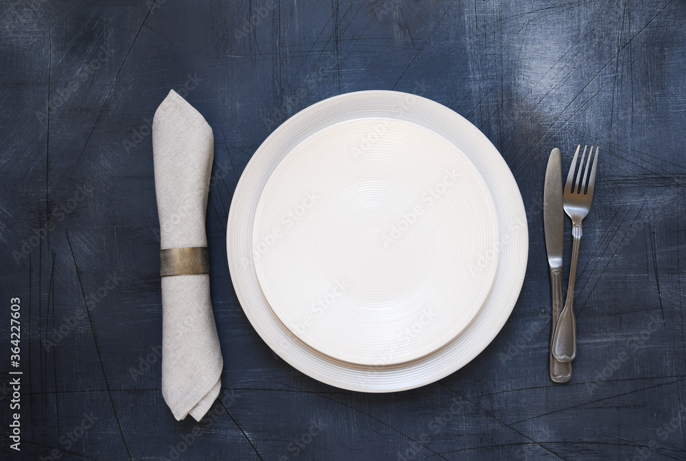 Table setting. White craft plate, cutlery and napkin on dark stone ...