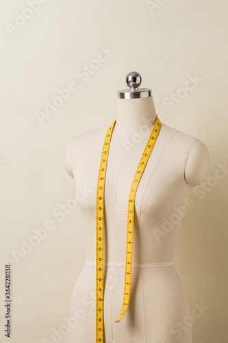 Women's clothing dummy with yellow measuring tape across neck.