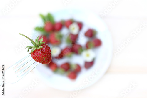 ripe strawberries on a fork on a background of blurred table silhouette with a bowl of berries top view. sweet breakfast dessert