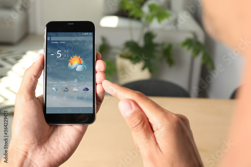Man using weather forecast app on smartphone indoors, closeup
