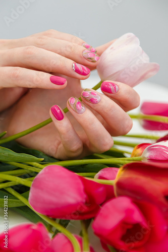Close up vertical shot of woman hands with spring manicure holding pink tulip on tulips bouquet background. Nail art  gel nail polish design concept.