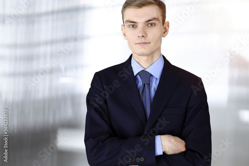 Young businessman in a suit, while standing in a sunny office. Business success concept nowadays