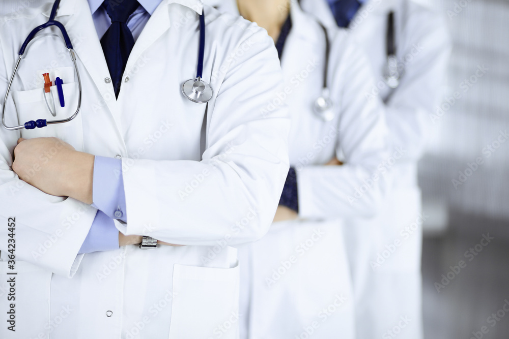 Group of modern doctors standing as a team with crossed arms and stethoscopes in hospital office. Physicians ready to examine and help patients. Medical help, insurance in health care, best desease Group of modern doctors standing as a team with crossed arms and stethoscopes in hospital office. Physicians ready to examine and help patients. Medical help, insurance in health care, best desease