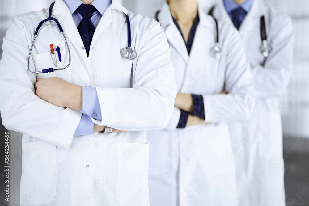 Group of modern doctors standing as a team with crossed arms and stethoscopes in hospital office. Physicians ready to examine and help patients. Medical help, insurance in health care, best desease Group of modern doctors standing as a team with crossed arms and stethoscopes in hospital office. Physicians ready to examine and help patients. Medical help, insurance in health care, best desease