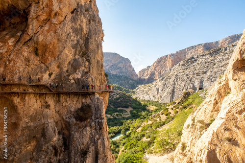 Mountain landscape view of El Chorro narrow gorge and El Caminito del Rey walkway wooden platforms attached to vertical rocks over the precipice, with people walking, Spain.