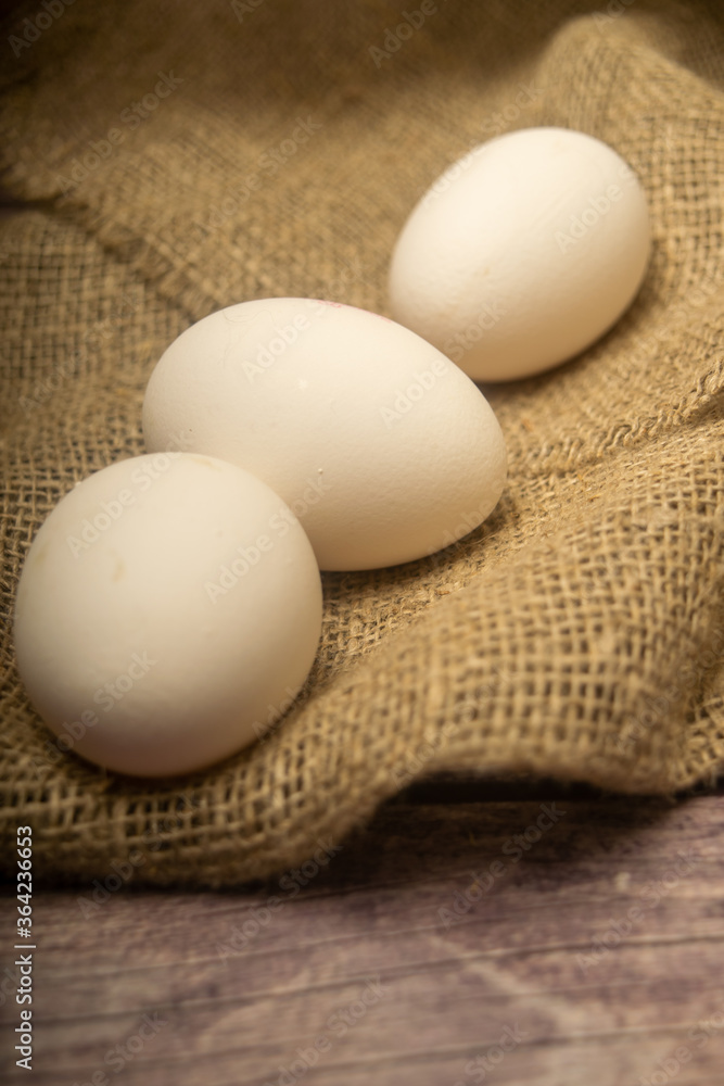 White chicken eggs on a background of homespun fabric with a rough texture. Close up. White chicken eggs on a background of homespun fabric with a rough texture. Close up.