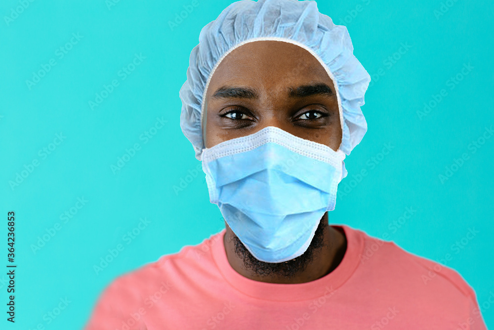 Portrait of a young african person wearing mask and hair cap for coronavirus protection looking at camera, against blue studio background Portrait of a young african person wearing mask and hair cap for coronavirus protection looking at camera, against blue studio background