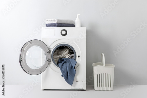 Washing machine with clothes and  laundry basket in front of gray wall. photo