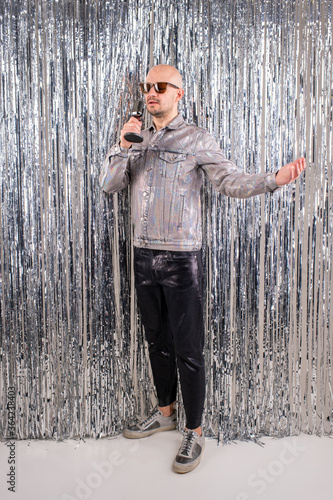 The 90s singer, wearing a silver shirt and leather pants, sings songs in the studio isolated on a glittering backdrop
