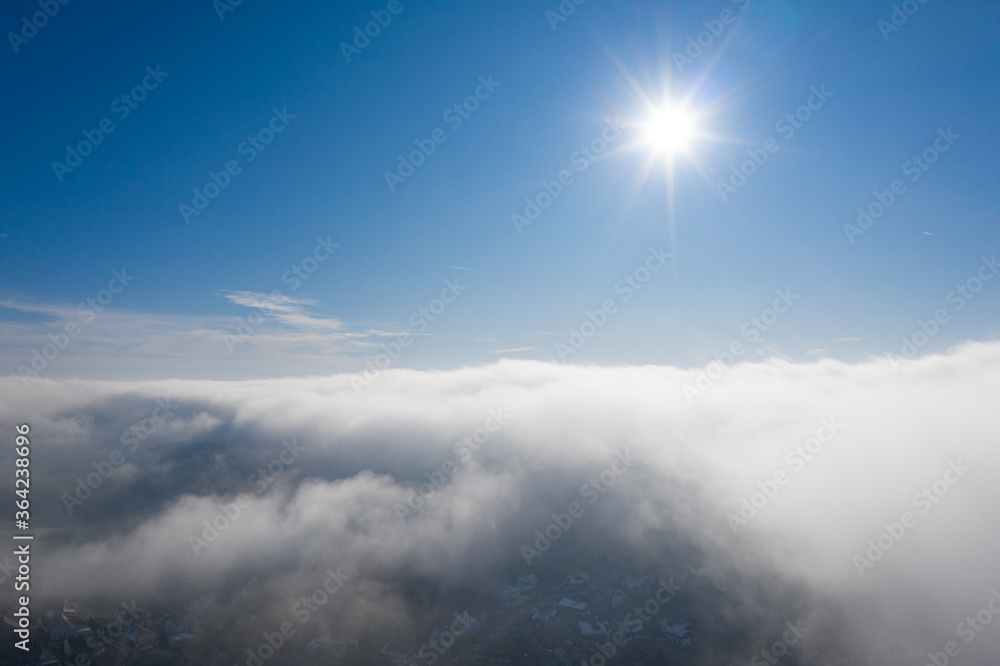 Nebelbank lichtet sich mit Sonne darüber und Gebäuden im Nebelloch - rechtszentriert
