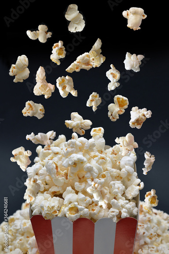 Flying popcorn in paper box on black background, top view