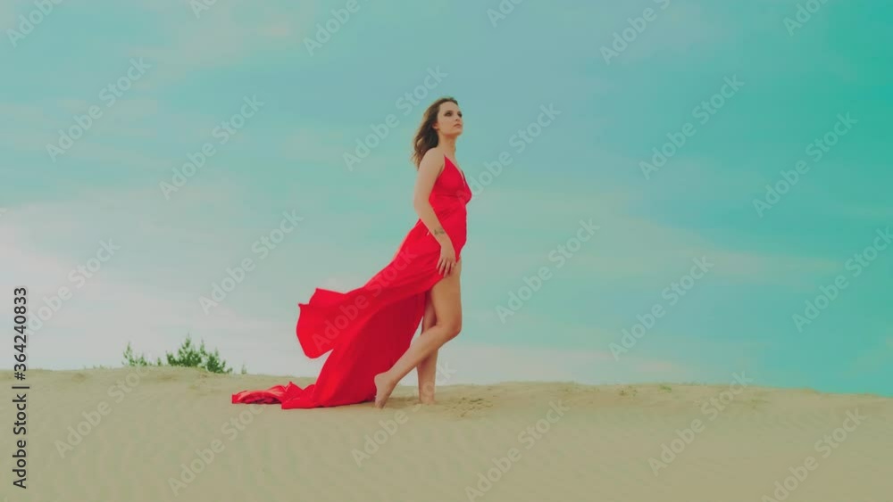 Passionate charming stylish woman posing model on backdrop sandy beach, oasis green coniferous trees, blue hot sky desert. Sexy bare legs. Girl brunette loose hair. Long red silk dress fluttering wind Passionate charming stylish woman posing model on backdrop sandy beach, oasis green coniferous trees, blue hot sky desert. Sexy bare legs. Girl brunette loose hair. Long red silk dress fluttering wind