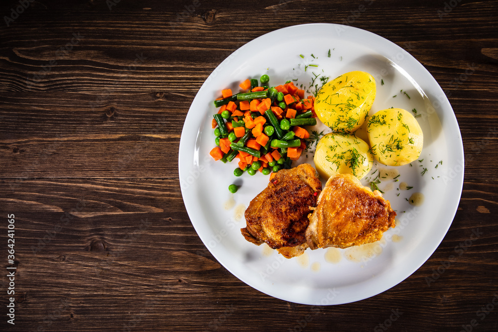 Roasted chicken thighs with boiled carrots, peas and potatoes on wooden background Roasted chicken thighs with boiled carrots, peas and potatoes on wooden background
