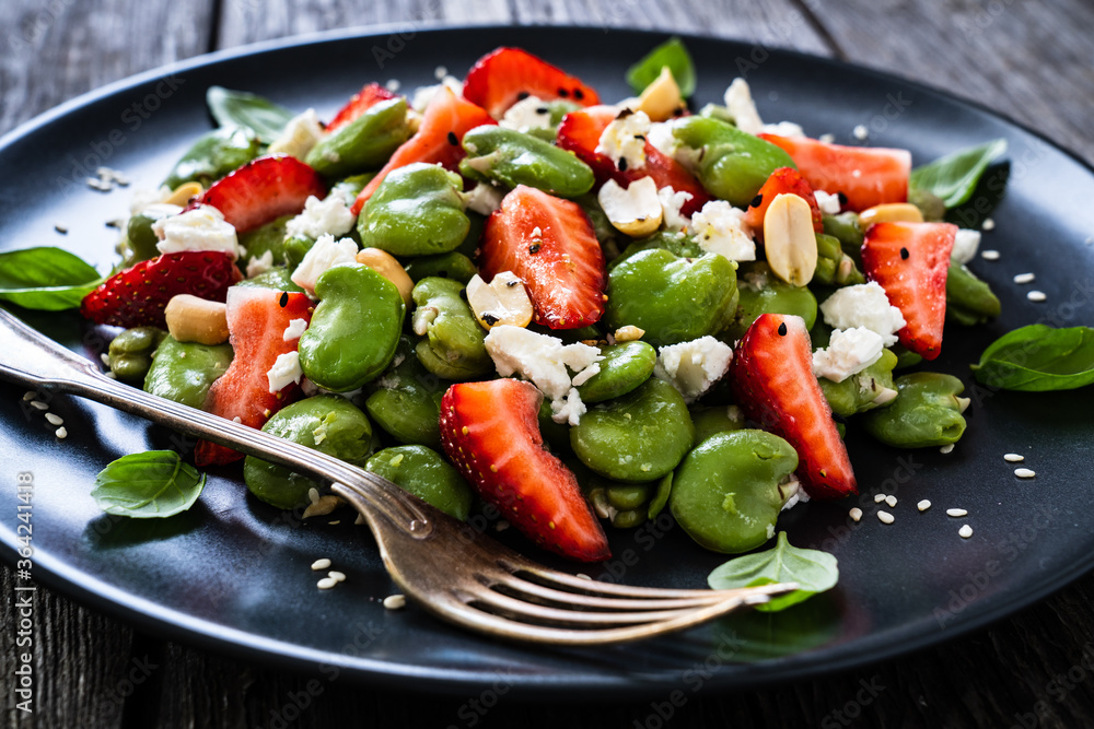 Broad beans salad with feta cheese and strawberries on wooden table
