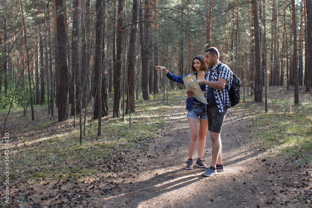 A young couple navigates the area using a map. Hiking in a pine forest A young couple navigates the area using a map. Hiking in a pine forest