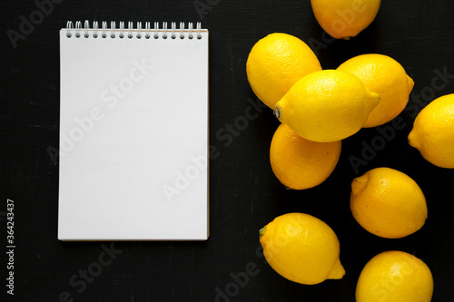 Ripe Yellow Organic Lemons and blank notepad on a black background, top view. Flat lay, overhead, from above. photo