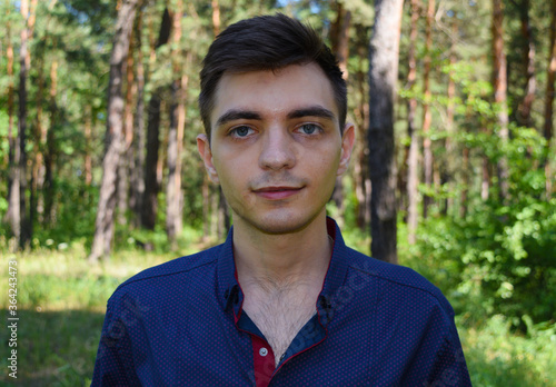 Portrait of a young handsome brunet man in shirt on forest background