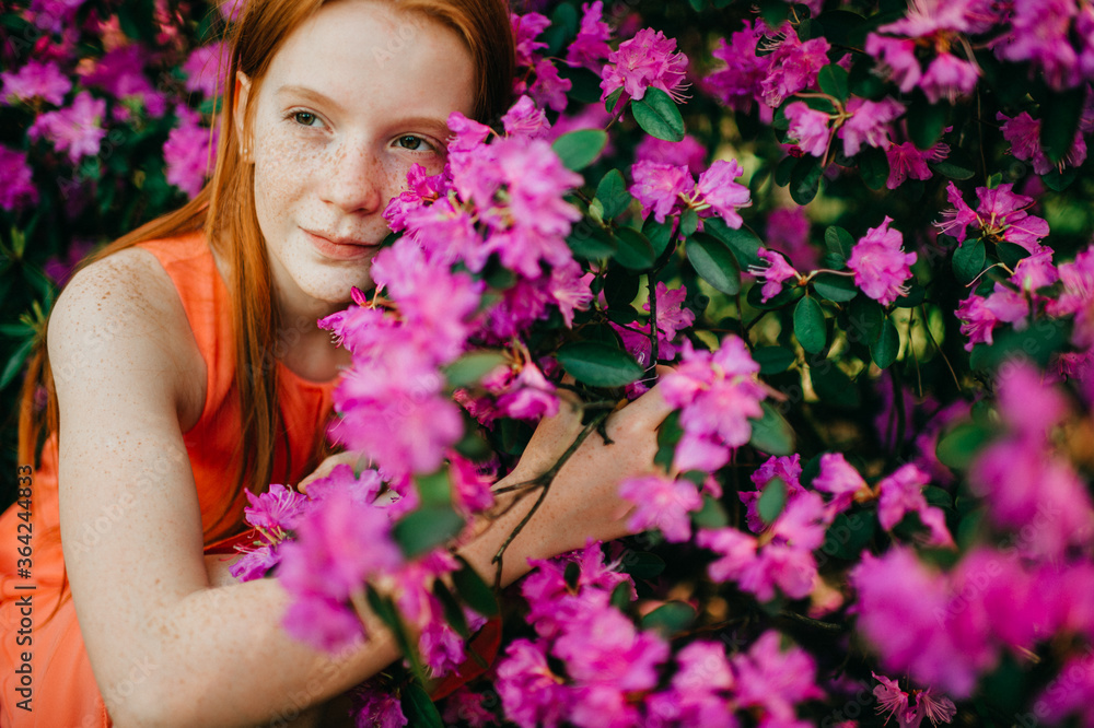 Naklejka premium Picture of an amazing red-haired baby girl in an orange dress enjoying a pastime in the big spring garden