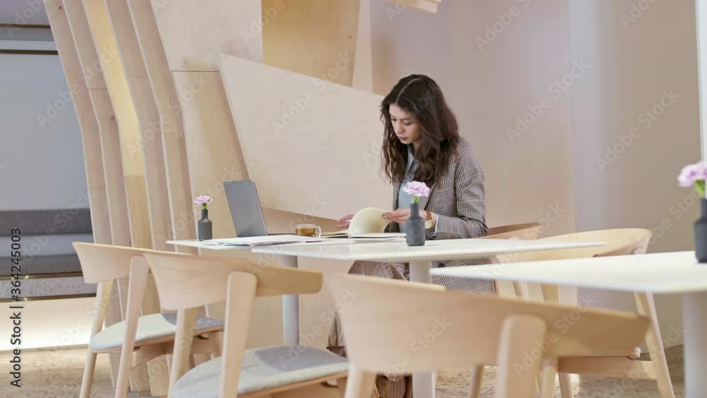 Medium shot of young Caucasian businesswoman with long curly hair sitting at workplace and looking through papers Medium shot of young Caucasian businesswoman with long curly hair sitting at workplace and looking through papers