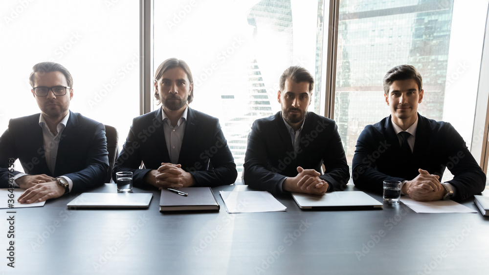 Group of focused male professional headhunters recruiters sitting at table, waiting for job candidate for interview. Serious hr managers teammates in formal wear looking at camera, hiring process. Group of focused male professional headhunters recruiters sitting at table, waiting for job candidate for interview. Serious hr managers teammates in formal wear looking at camera, hiring process.