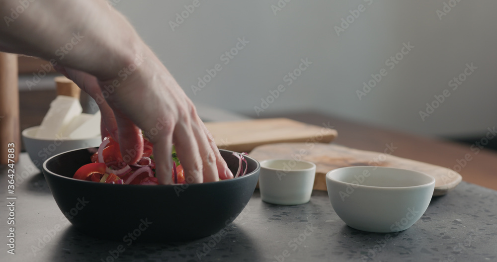 man mixing greek salad in black bowl with wood servers man mixing greek salad in black bowl with wood servers