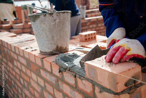 A man lays bricks. Mason is building a wall. Brick wall. The erection of a brick wall. Trowel, cement and brick in the hands of a man.