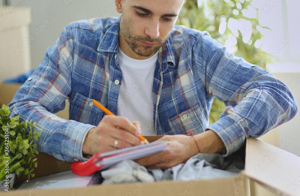 A moving man sitting on the floor in empty apartment, Among the Boxes, Checking the List of Things A moving man sitting on the floor in empty apartment, Among the Boxes, Checking the List of Things