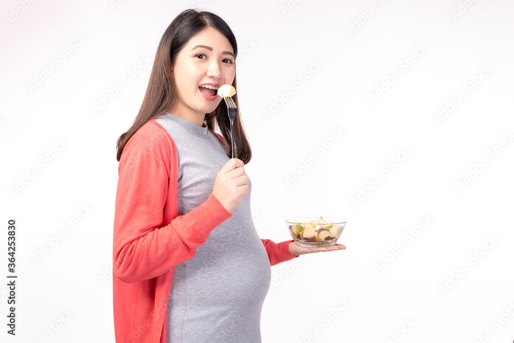 Pregnant young asian woman eating fruit salad fresh, Fruit salad is healthy food for baby or fetus. Pregnant mother hold blow of fruit salad. Pregnancy, health care concept White backdrop Pregnant young asian woman eating fruit salad fresh, Fruit salad is healthy food for baby or fetus. Pregnant mother hold blow of fruit salad. Pregnancy, health care concept White backdrop