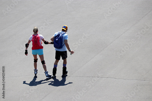 Couple riding on roller skates on a street holding hands, top view. Summer leisure in a city, healthy lifestyle