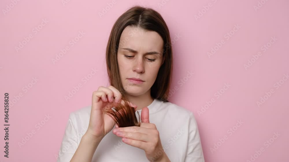 Depressed young woman looking at split ends, isolated on pink studio background. Female hormone problems or vitamin deficiency. Unhappy girl feels upset about brittle damaged dry hair loss concept Depressed young woman looking at split ends, isolated on pink studio background. Female hormone problems or vitamin deficiency. Unhappy girl feels upset about brittle damaged dry hair loss concept