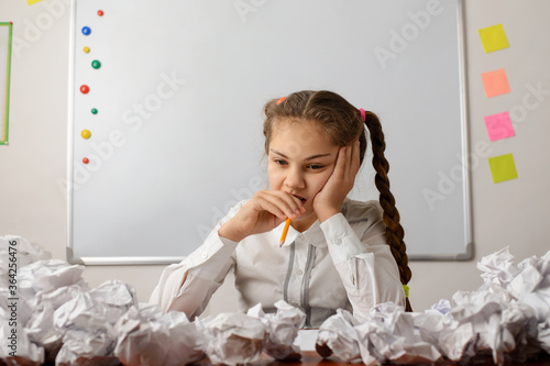 Concept of thinking hard. Small dipressed girl near the whiteboard thinking about the composition, have no idea to start with, failed many times to write a text photo