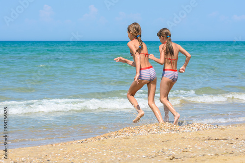 Two girls run along the shore running into the sea