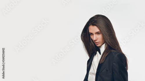 Fashion portrait of androgynous beautiful man with perfect glossy long hair wearing black suit and bow tie. Glamour feminine attractive model with healthy and brown hair. Stylish vogue 