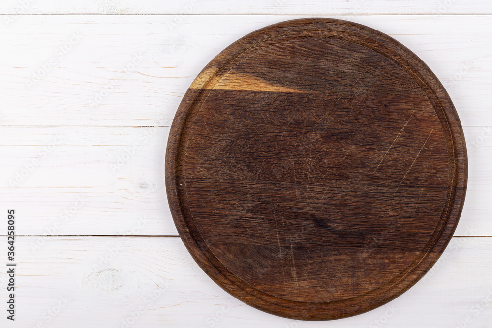 Brown round cutting board on a white wooden background. View from above. Brown round cutting board on a white wooden background. View from above.
