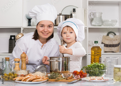 Portrait of smiling woman with her daughter who are satisfied of cooking soup in the kitchen at home.