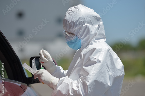 Unrecognizable people wearing protective suit handles a pharyngeal exudate/ swab collection kit for the coronavirus. Test tube for taking OP NP patient specimen sample, PCR DNA testing