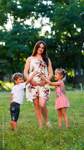Pregnant mother with long hair with two little children posing in the park.