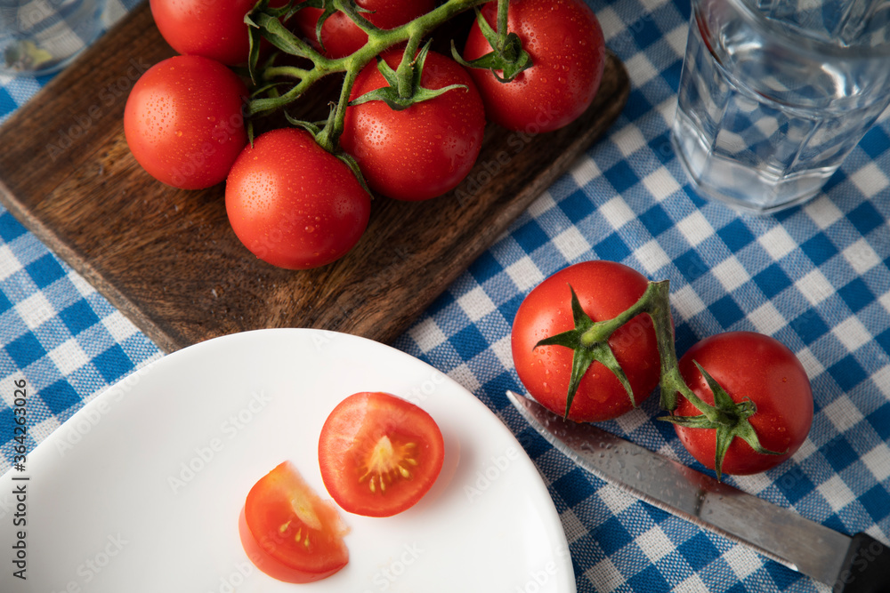 Fresh red tomatoes with water drops on a table covered with a blue tablecloth Fresh red tomatoes with water drops on a table covered with a blue tablecloth