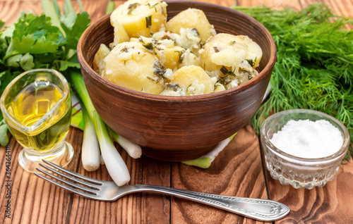 Bowl with boiled potatoes with greenery, oil and salt on wooden background.