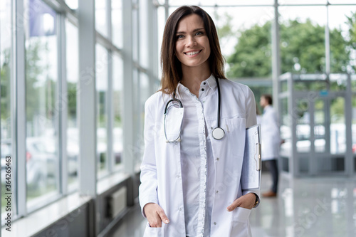 Canvas-taulu Portrait of young woman doctor with white coat standing in hospital