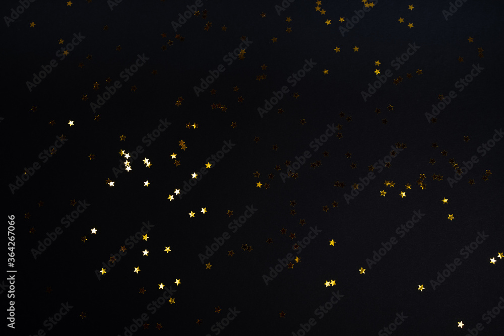 Fototapeta premium Black contrast color festive background with golden stars glitter confetti. Flat lay style with copy space for text, design. Trendy Holiday concept. Perfect backdrop for social media, blog, postcard