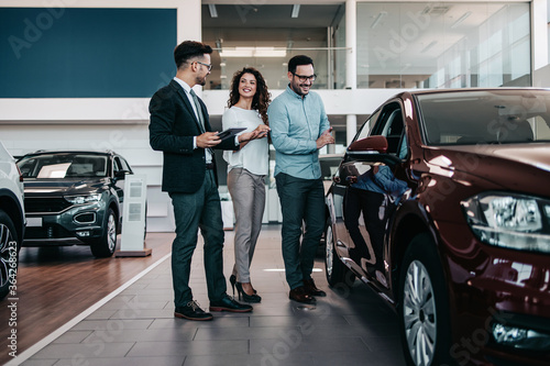 Middle age couple choosing and buying car at car showroom. Car salesman helps them to make right decision.