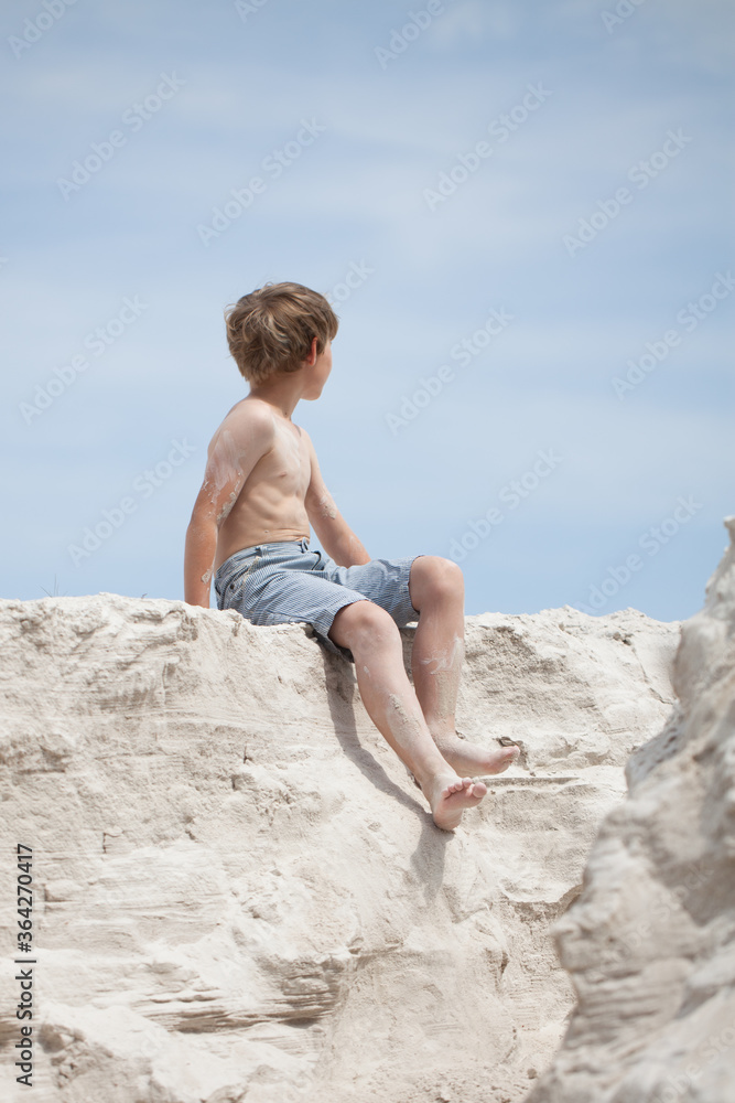 A boy sitting on the sand and looking at the blue sky