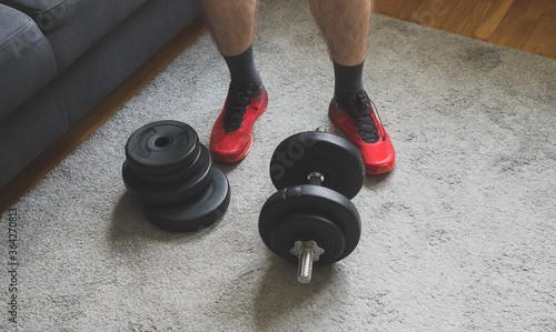 Man standing near adjustable dumbbell with plates at home. photo